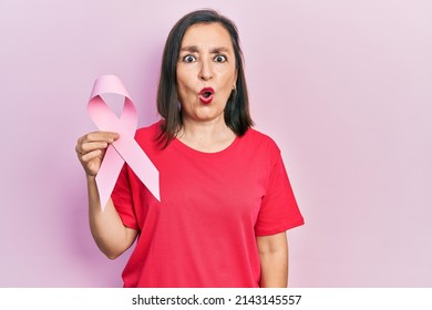 Middle age hispanic woman holding pink cancer ribbon scared and amazed with open mouth for surprise, disbelief face  - Powered by Shutterstock