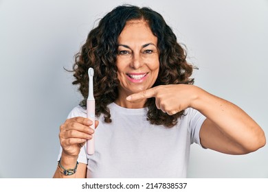 Middle Age Hispanic Woman Holding Electric Toothbrush Smiling Happy Pointing With Hand And Finger 