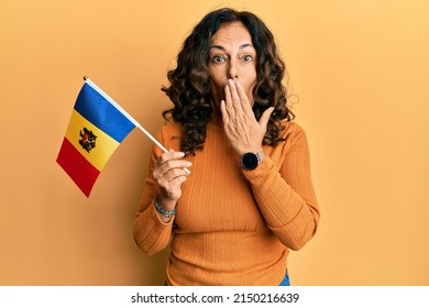 Middle age hispanic woman holding moldova flag covering mouth with hand, shocked and afraid for mistake. surprised expression 