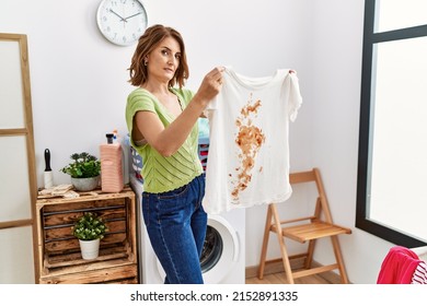 Middle Age Hispanic Woman Holding Dirty T Shirt At Laundry Room