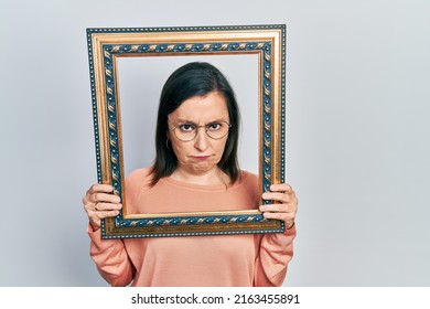 Middle Age Hispanic Woman Holding Empty Frame Depressed And Worry For Distress, Crying Angry And Afraid. Sad Expression. 