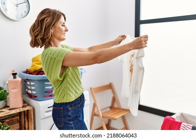 Middle Age Hispanic Woman Holding Dirty T Shirt At Laundry Room