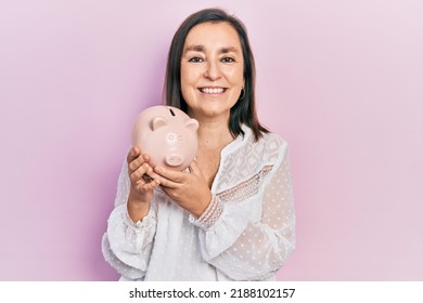 Middle age hispanic woman holding piggy bank smiling with a happy and cool smile on face. showing teeth. 
