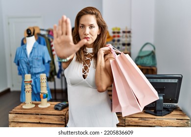 Middle Age Hispanic Woman Holding Shopping Bags At Retail Shop Doing Stop Sing With Palm Of The Hand. Warning Expression With Negative And Serious Gesture On The Face. 