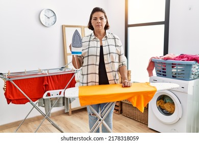 Middle Age Hispanic Woman Ironing Clothes At Home Thinking Attitude And Sober Expression Looking Self Confident 