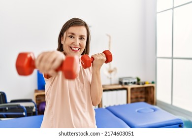 Middle Age Hispanic Woman Lifting Weights At Physiotherapy Clinic