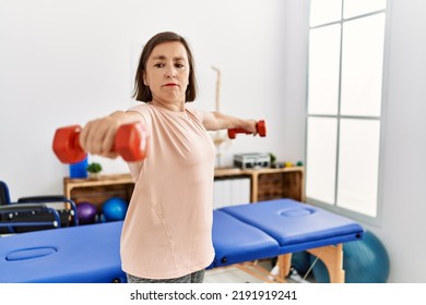 Middle Age Hispanic Woman Lifting Weights At Physiotherapy Clinic