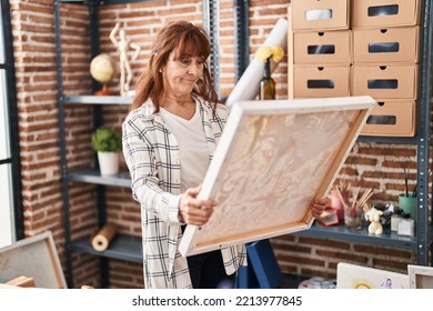 Middle Age Hispanic Woman Looking At Painter Canvas Relaxed With Serious Expression On Face. Simple And Natural Looking At The Camera. 