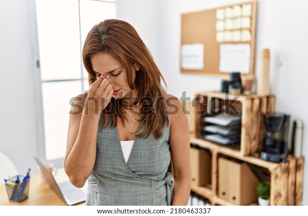 Middle age hispanic woman at the office tired rubbing\
nose and eyes feeling fatigue and headache. stress and frustration\
concept. 