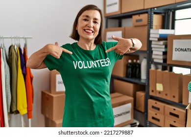 Middle Age Hispanic Woman Pointing To Volunteer Tshirt At Donations Stand