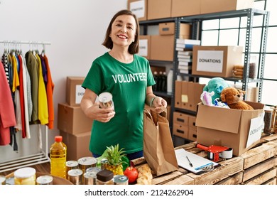Middle age hispanic woman preparing bag with groceries at donations stand - Shutterstock ID 2124262904