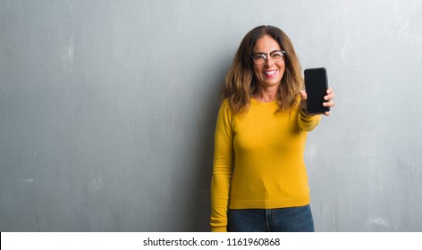 Middle Age Hispanic Woman Showing Smarphone Screen With A Happy Face Standing And Smiling With A Confident Smile Showing Teeth