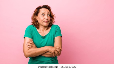 middle age hispanic woman shrugging, feeling confused and uncertain, doubting with arms crossed and puzzled look - Powered by Shutterstock