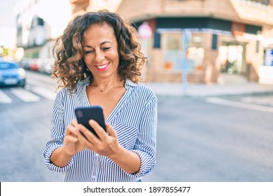 Middle Age Hispanic Woman Smiling Happy And Using Smartphone At The City.