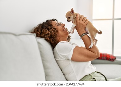 Middle age hispanic woman smiling confident holding chihuahua at home