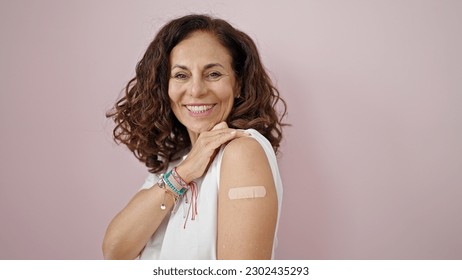 Middle age hispanic woman smiling confident standing with band aid on arm over isolated pink background - Powered by Shutterstock