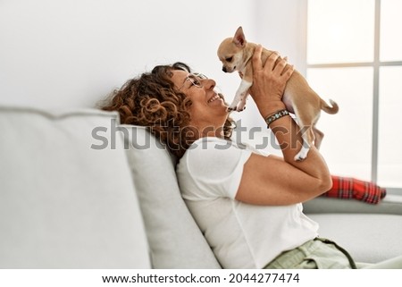 Middle age hispanic woman smiling confident holding chihuahua at home