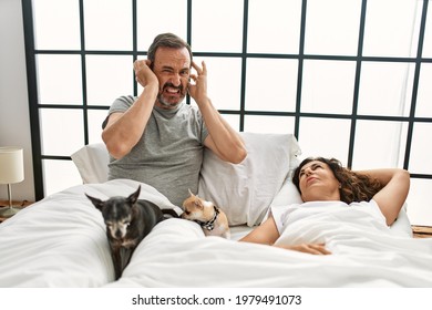 Middle Age Hispanic Woman Snoring And Man Angry Covering Ears At Bedroom.