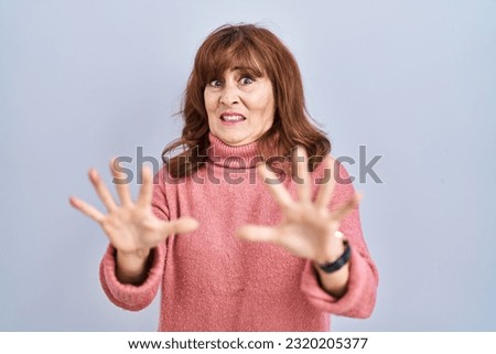 Middle age hispanic woman standing over isolated background afraid and terrified with fear expression stop gesture with hands, shouting in shock. panic concept. 