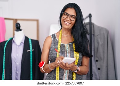 Middle age hispanic woman tailor smiling confident writing on notebook at tailor shop - Powered by Shutterstock