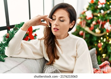 Middle Age Hispanic Woman Taking Pill Sitting By Christmas Tree At Home