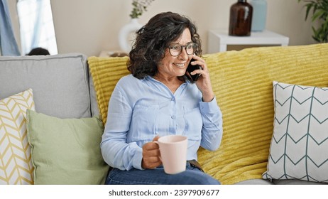 Middle age hispanic woman talking on smartphone drinking coffee at home - Powered by Shutterstock