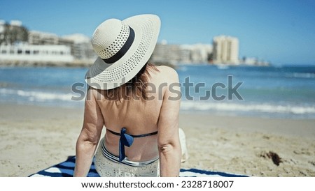 Middle age hispanic woman tourist sunbathing sitting on the towel at the beach