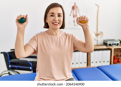 Middle age hispanic woman training hands strength with small balls at physiotherapy clinic - Powered by Shutterstock