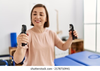 Middle age hispanic woman training hands strength with hand grip at physiotherapy clinic - Shutterstock ID 2178710941