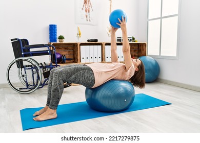 Middle Age Hispanic Woman Training With Pilates Ball At Physiotherapy Clinic