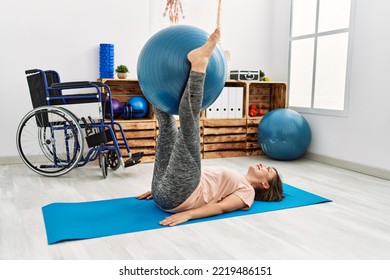 Middle Age Hispanic Woman Training With Pilates Ball At Physiotherapy Clinic