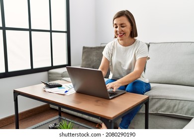 Middle Age Hispanic Woman Using Laptop Doing Domestic Finances At Home