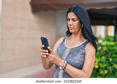 Middle Age Hispanic Woman Using Smartphone With Serious Expression At Street