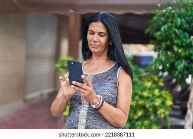 Middle Age Hispanic Woman Using Smartphone With Serious Expression At Street