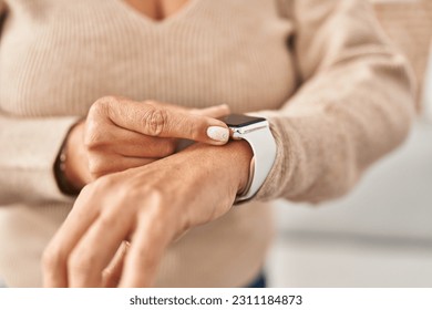 Middle age hispanic woman using smartwatch standing at home - Shutterstock ID 2311184873
