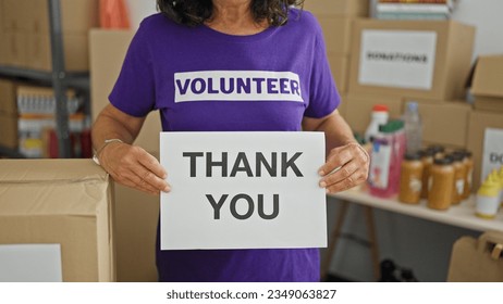 Middle age hispanic woman volunteer holding thank you message at charity center