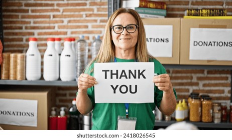 Middle age hispanic woman volunteer holding thank you message on paper at charity center
