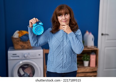 Middle Age Hispanic Woman Waiting For Laundry Serious Face Thinking About Question With Hand On Chin, Thoughtful About Confusing Idea 