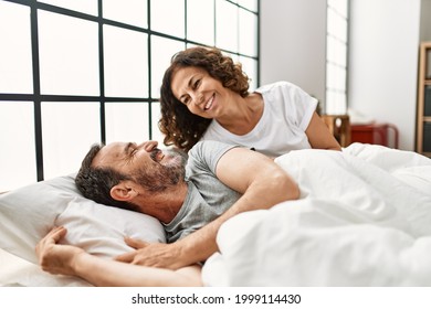 Middle age hispanic woman waking up her husband lying on the bed at home. - Powered by Shutterstock