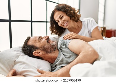 Middle age hispanic woman waking up her husband lying on the bed at home. - Powered by Shutterstock