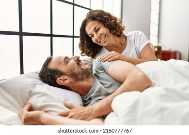 Middle age hispanic woman waking up her husband lying on the bed at home. - Powered by Shutterstock