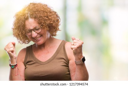 Middle age hispanic woman wearing glasses over isolated background very happy and excited doing winner gesture with arms raised, smiling and screaming for success. Celebration concept.
