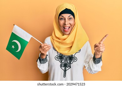 Middle Age Hispanic Woman Wearing Hijab Holding Pakistan Flag Smiling Happy Pointing With Hand And Finger To The Side 