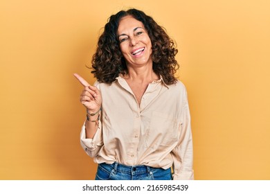 Middle Age Hispanic Woman Wearing Casual Clothes With A Big Smile On Face, Pointing With Hand And Finger To The Side Looking At The Camera. 