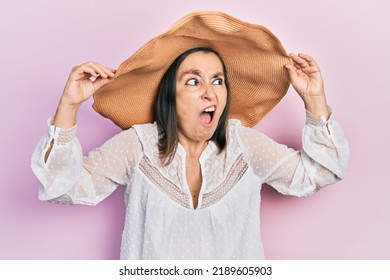 Middle Age Hispanic Woman Wearing Summer Hat Angry And Mad Screaming Frustrated And Furious, Shouting With Anger. Rage And Aggressive Concept. 