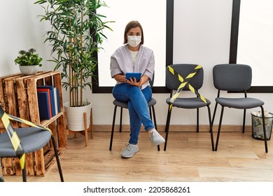 Middle Age Hispanic Woman Wearing Safety Mask Using Tablet At Waiting Room