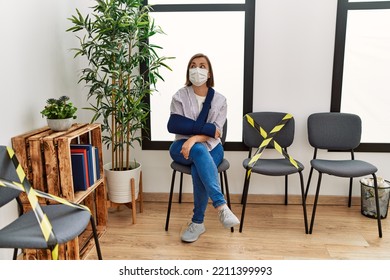 Middle Age Hispanic Woman Wearing Safety Mask Wearing Arm Sling At Waiting Room