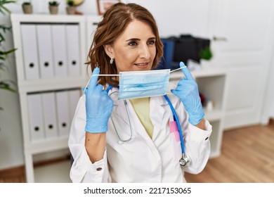 Middle Age Hispanic Woman Wearing Doctor Uniform Holding Medical Mask At Clinic