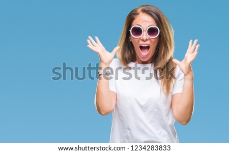 Middle age hispanic woman wearing fashion sunglasses over isolated background celebrating crazy and amazed for success with arms raised and open eyes screaming excited. Winner concept