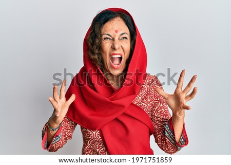 Middle age hispanic woman wearing tradition sherwani saree clothes crazy and mad shouting and yelling with aggressive expression and arms raised. frustration concept. 